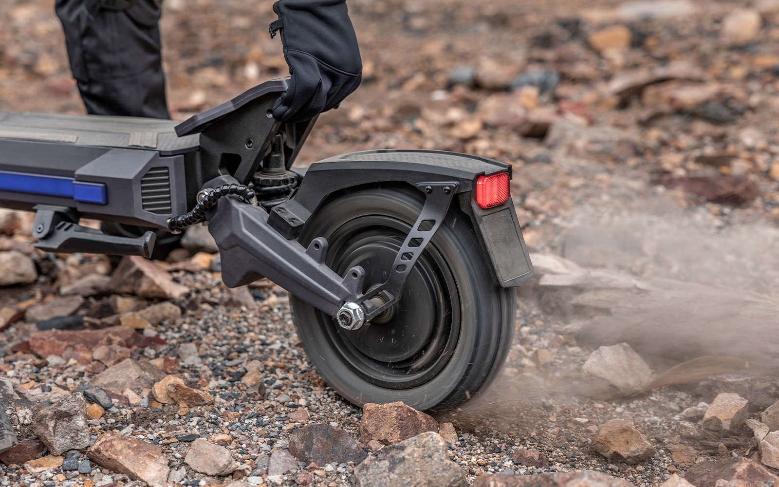 Ausom DT2 Pro electric scooter rear wheel kicking up dirt while accelerating up a steep dirt path, demonstrating high torque.